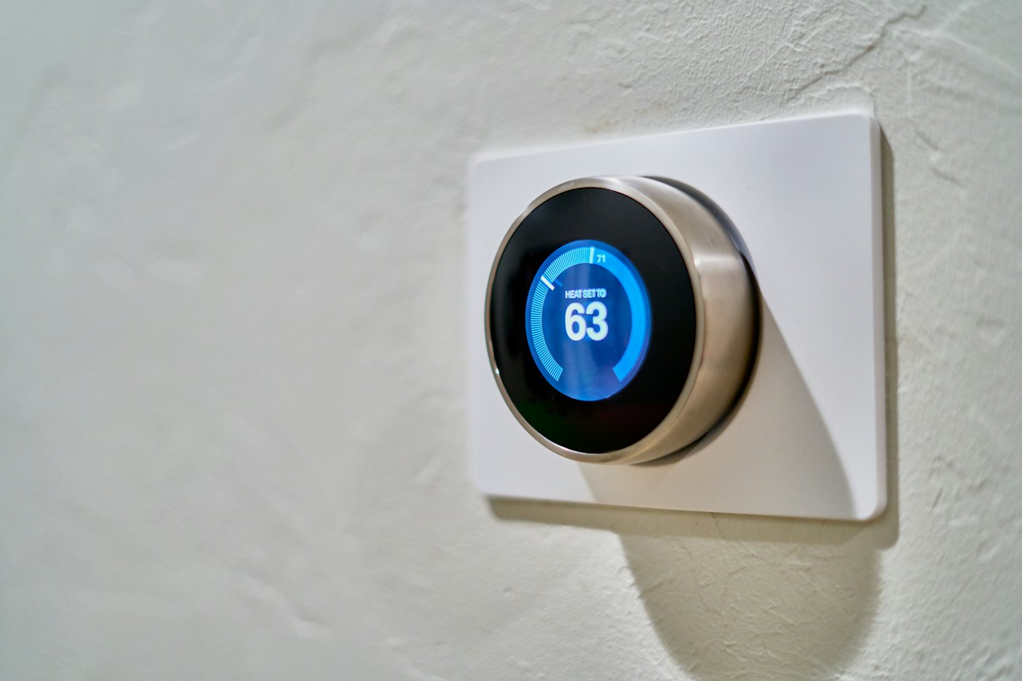 Modern smart thermostat showing heat setting on a white wall.