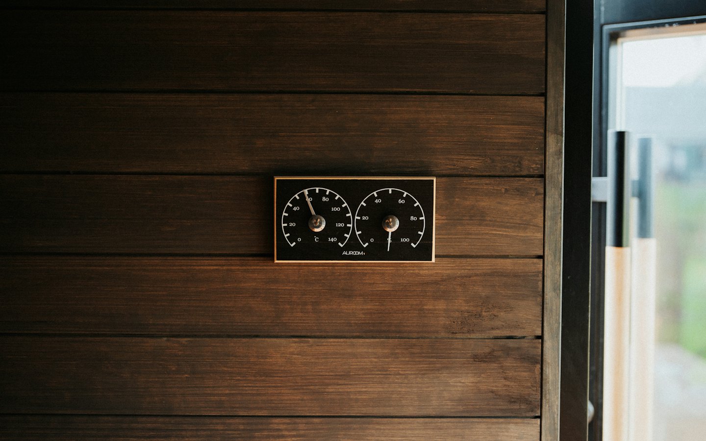 Black and gold thermometer mounted on a wooden wall.