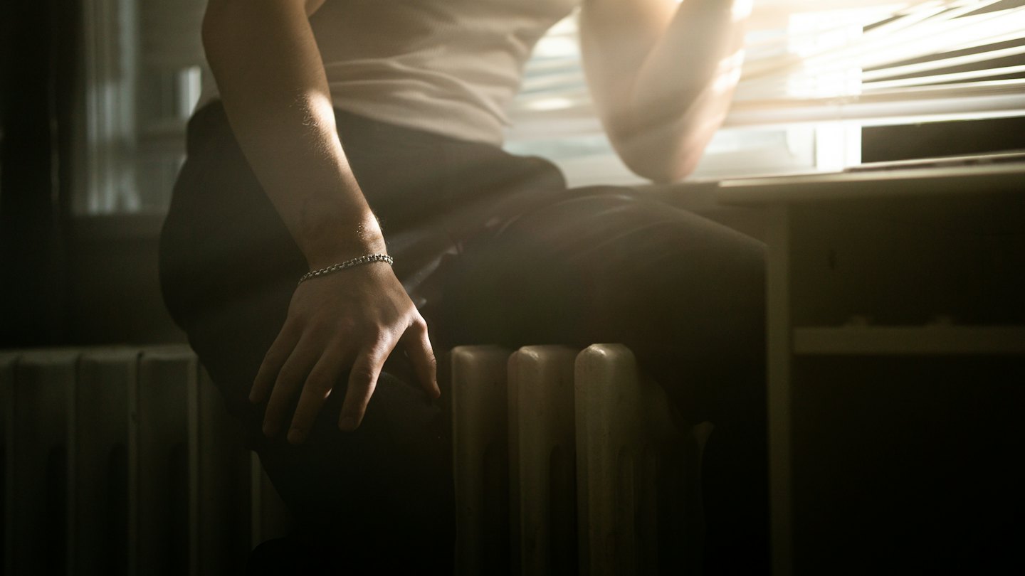 Person sitting next to a window with their hand resting on their thigh.