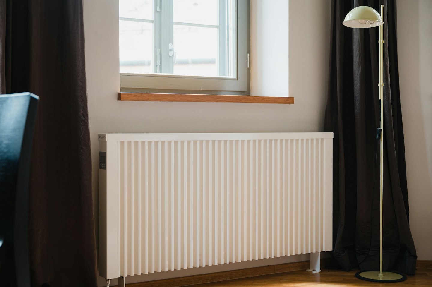 Modern white radiator under a window with wooden sill.