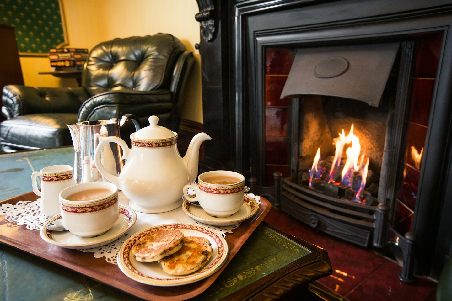Tea set and cakes on a tray by a fireplace.