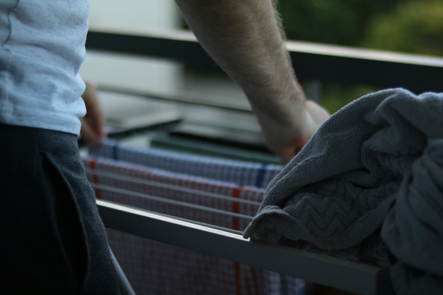 A person hangs striped laundry on a white drying rack.